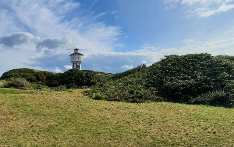 Der Wassertum der Insel Langeoog. Das Wahrzeichen der Insel. Wassertum auf Langeoog vor blauem Himmel und hinter grünen Dünen im Sommer
